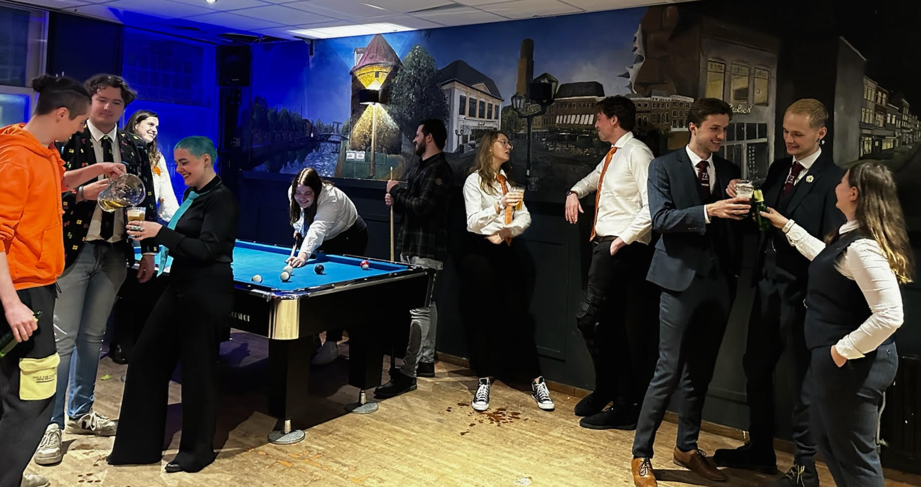 unnamed Groep studenten die gezellig samenkomen op de sociëteit met een muurschildering op de achtergrond. Sommigen spelen pool, anderen genieten van een drankje en dat in speciale commissie kleding.
